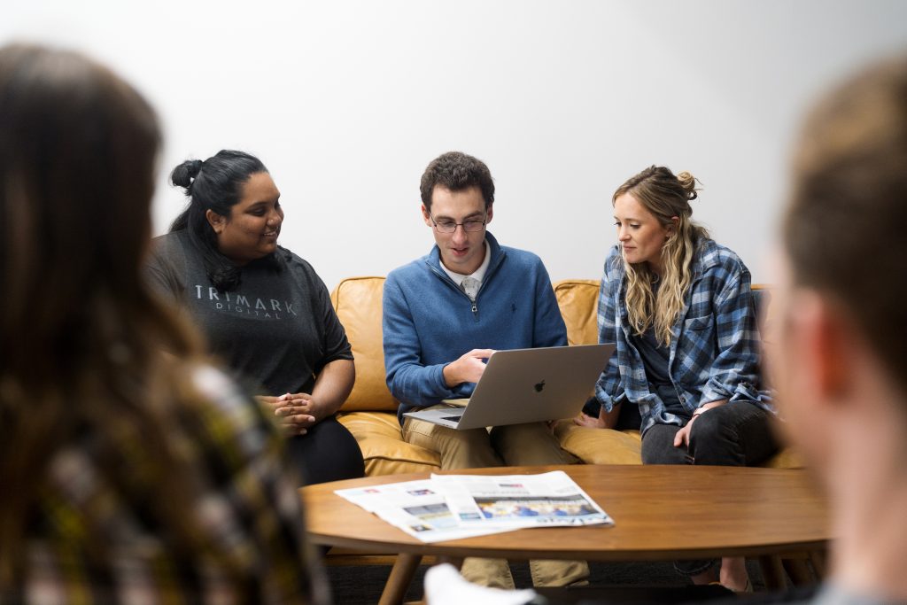 Three people sitting on a couch looking at a laptop