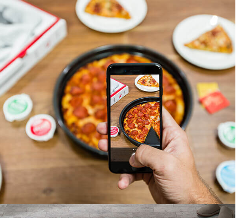 Person using a phone to take a photo of a Papa John's pizza with a slice taken out.
