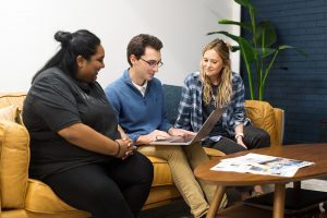 Three people looking at a laptop on a sofa