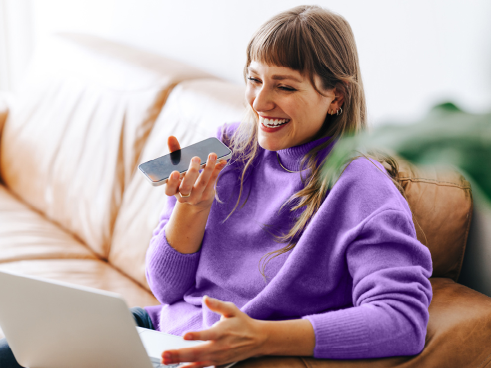 Photo of woman in her phone with her computer sitting on the couch