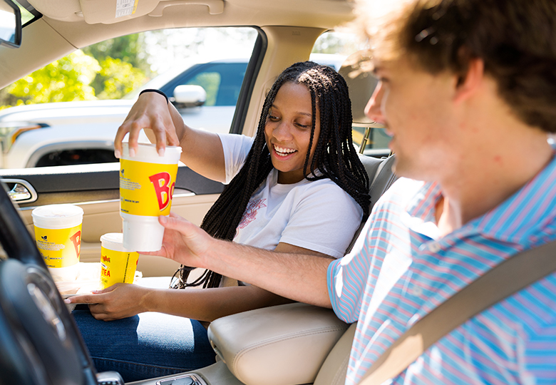 photo advertising Bojangles. Man and woman inside car passing each other beverages